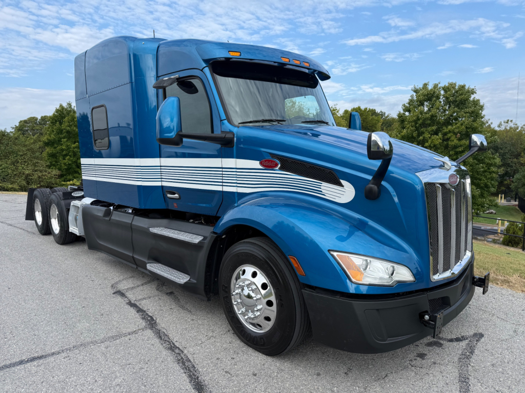 Peterbilt 579 truck in blue with sleeper cab, side stripes, and chrome wheels, front angled view.