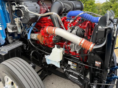 Peterbilt 579 engine bay showing red engine, blue hoses, and white coolant reservoir with surrounding components.