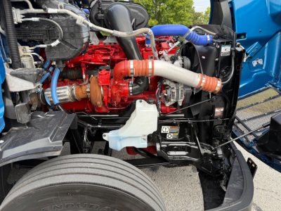 Peterbilt 579 engine bay showing red diesel engine, white coolant reservoir, blue hose, and black radiator support.