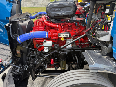 Peterbilt 579 engine bay showing red Cummins 12.0L engine with blue radiator hose, air intake, filters, and surrounding components.