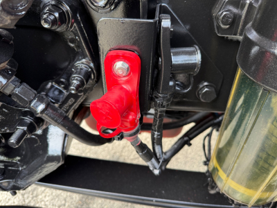 Peterbilt 579 engine bay view showing red battery disconnect switch with red cap, nearby hoses and metal brackets