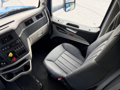 Peterbilt 579 truck interior, driver seat and dashboard visible with control panels, cup holders, and window view.