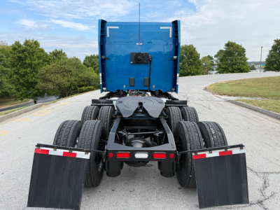 Peterbilt 579 chassis viewed from rear, blue sleeper cab in distance, dual rear wheels, fifth wheel, mudflaps, and tail lights visible