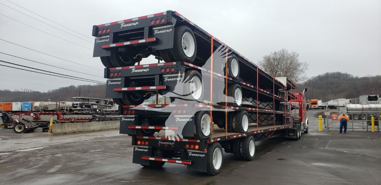 Transcraft DTL-2100 lowboy trailer stacked in yard with multiple axles and black color; visible branding and spare tires on rear; posted information includes VIN 1TTE482S6P3354884 and stock 48-6064