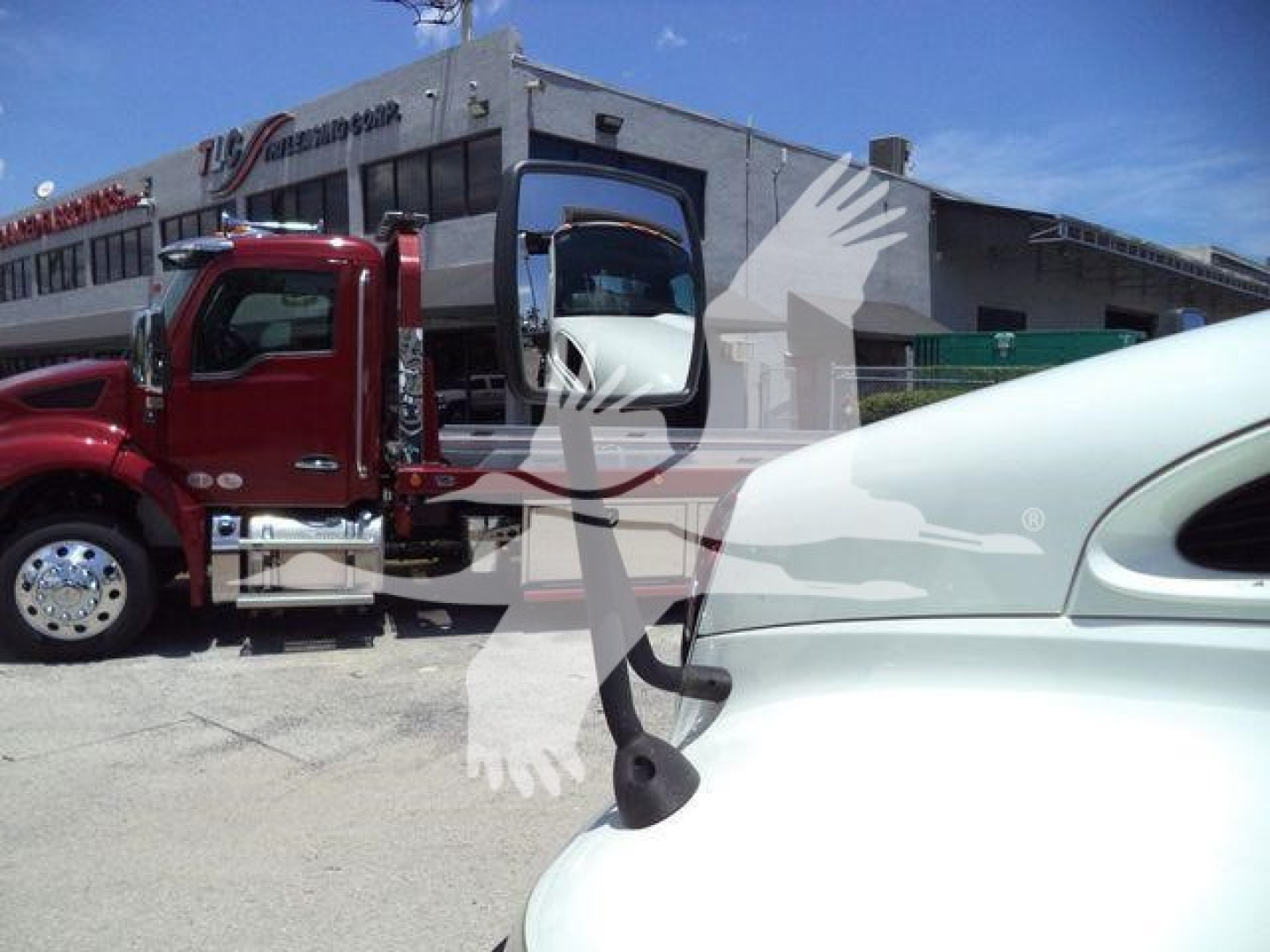 Truck cab and part of a white hood in foreground with red International MV rolloff truck in background.