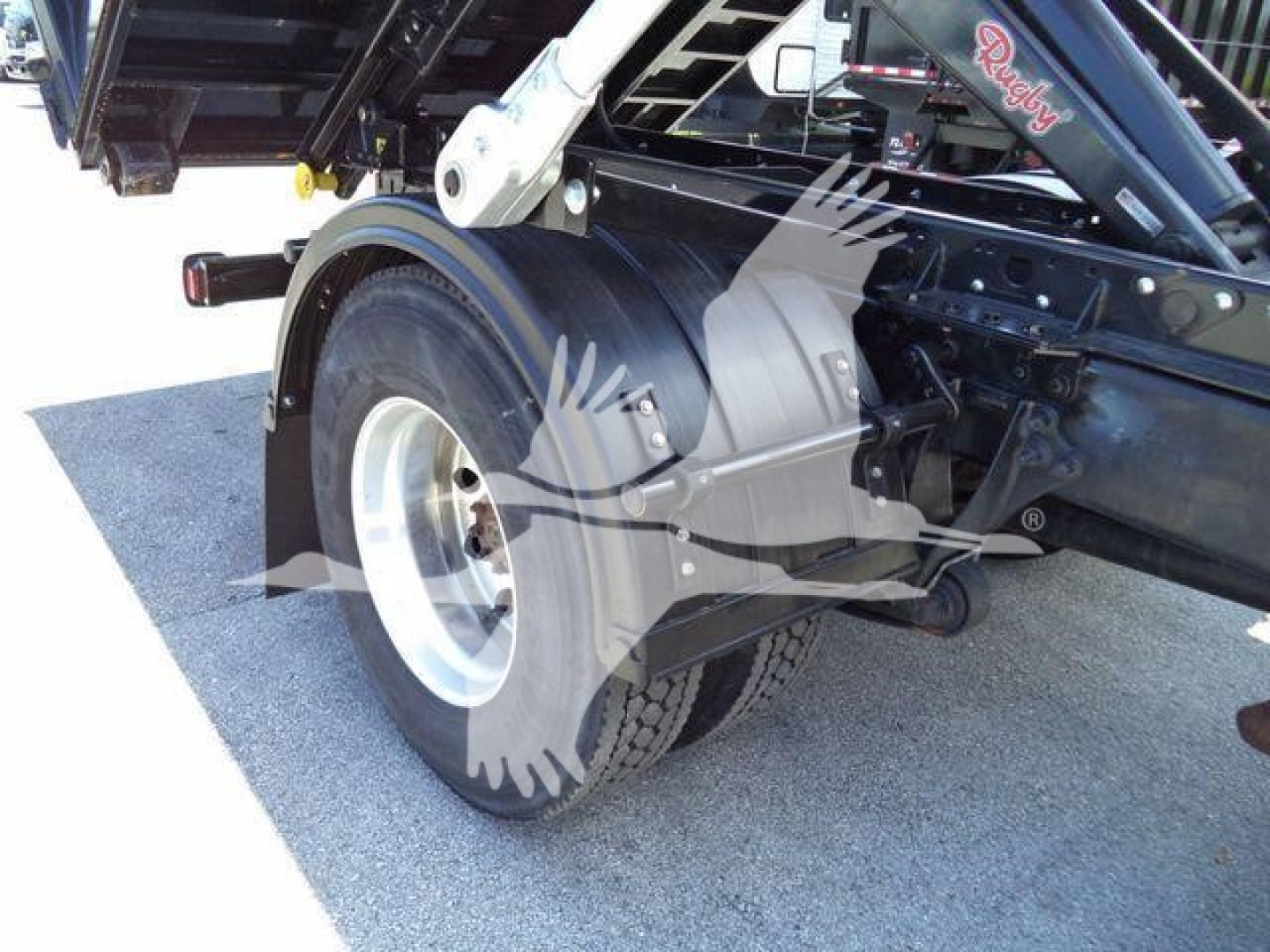 Truck chassis rear wheel and hoist arm visible with black frame and label 'Rooldy' on boom, wheel treads and white rim.