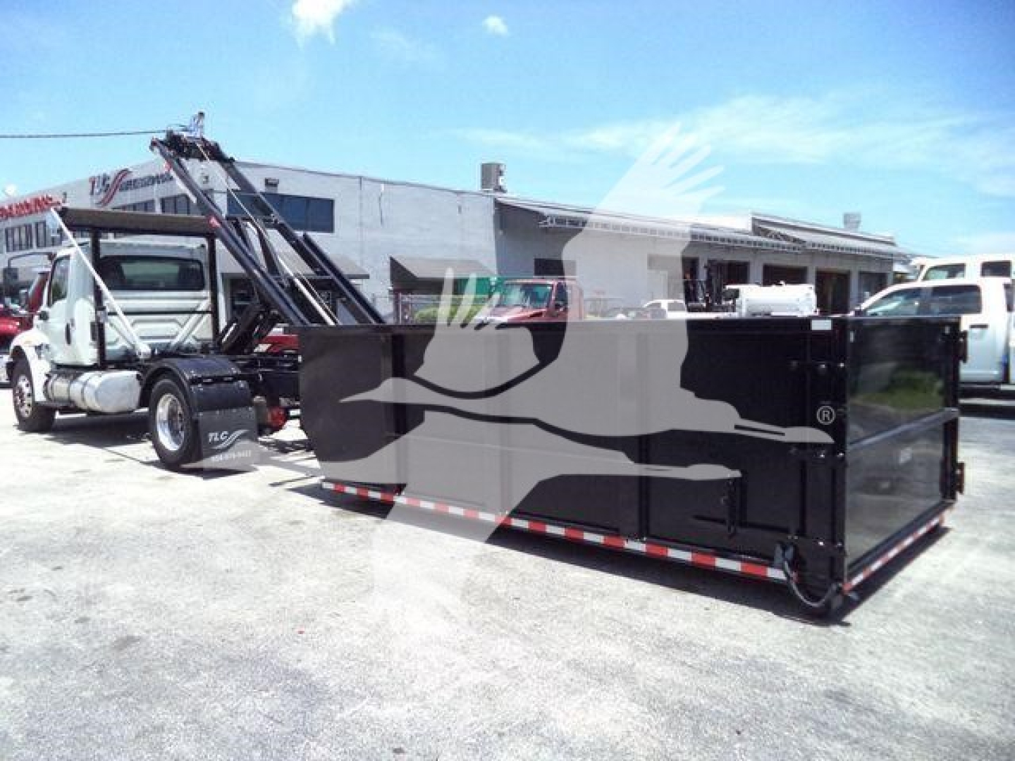 2020 International MV roll-off truck with large black dumpster container attached to truck, side view showing hydraulic crane and long bed.