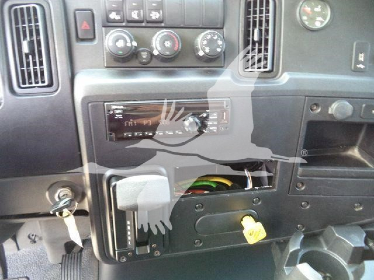 Interior of 2020 International MV rolloff truck dashboard with exposed component panel and yellow key. Visible controls include HVAC knobs, vents, and an empty stereo slot.