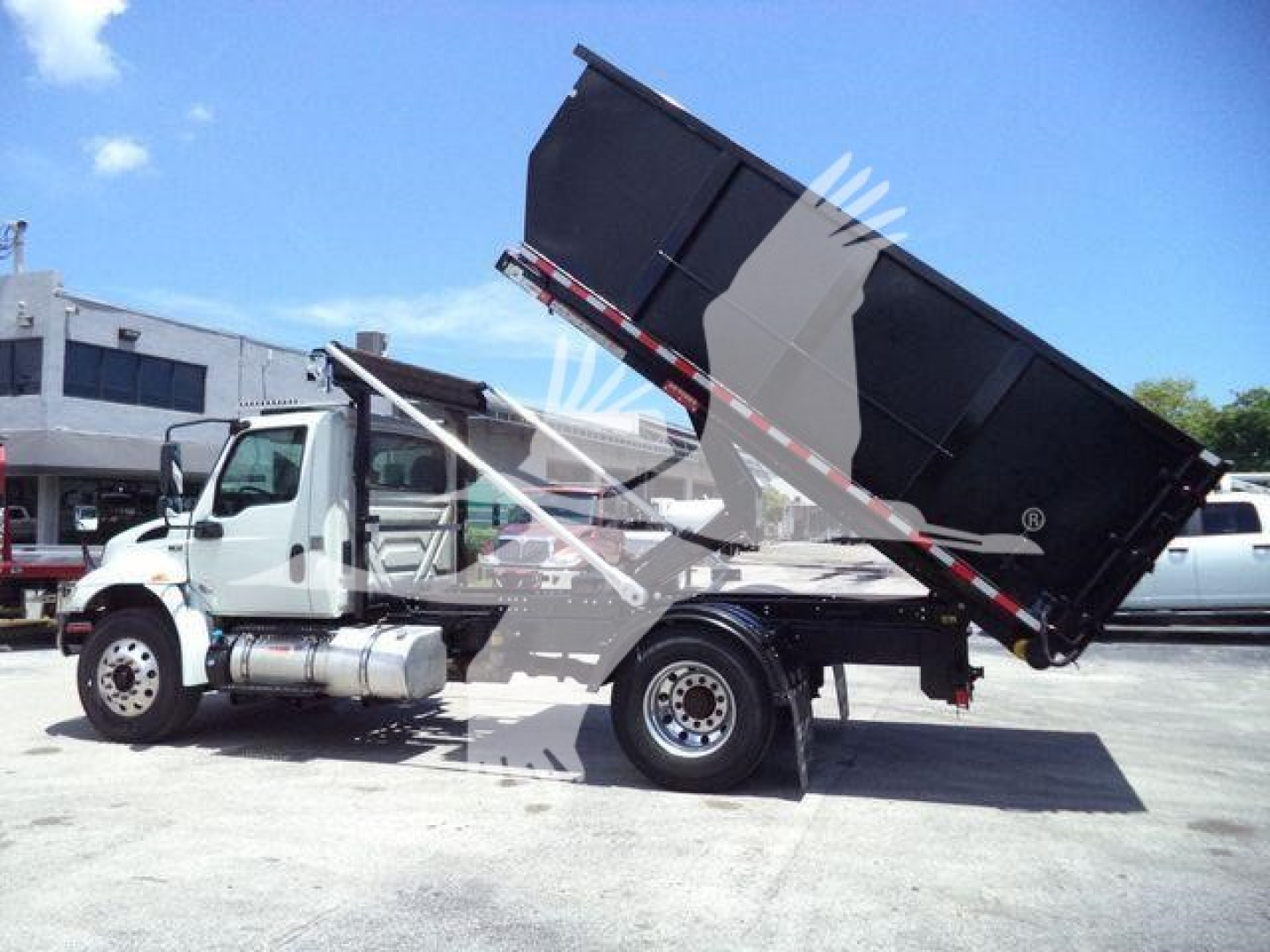 Dump truck with raised black dump bed in service position, International MV series, side view.