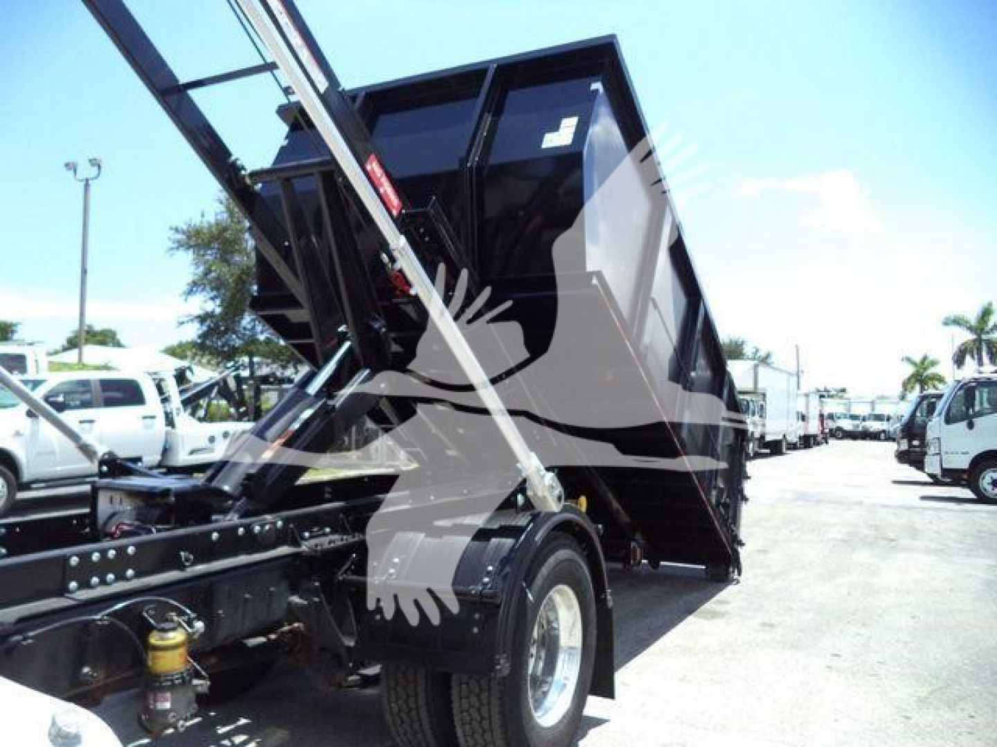 Dump truck chassis with raised dump bed and hydraulic cylinder in the process of dumping; rear wheel, chassis, and hydraulic components visible.