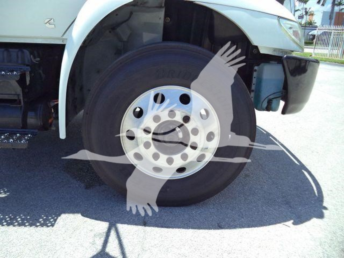 Front wheel and tire of a truck with visible Bridgestone tire and hub, fender and undercarriage of a white International MV roll-off truck.
