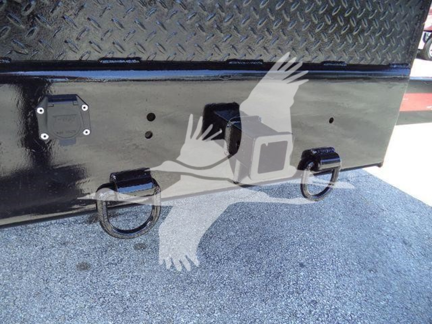 Truck rear showing two tow rings and a step area on a black metal surface with diamond plate top; circular latches and a recessed handle visible.