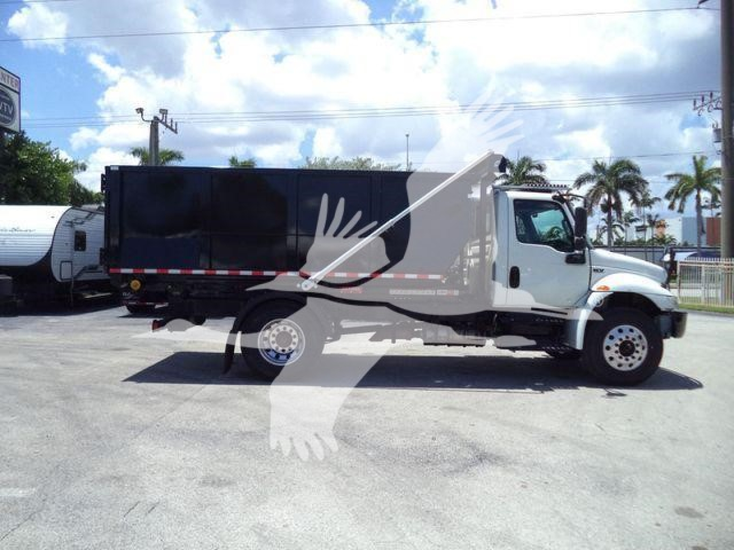 International MV roll-off truck in a parking lot, side view showing black dump body with white cab and red/white reflective stripe along the side.