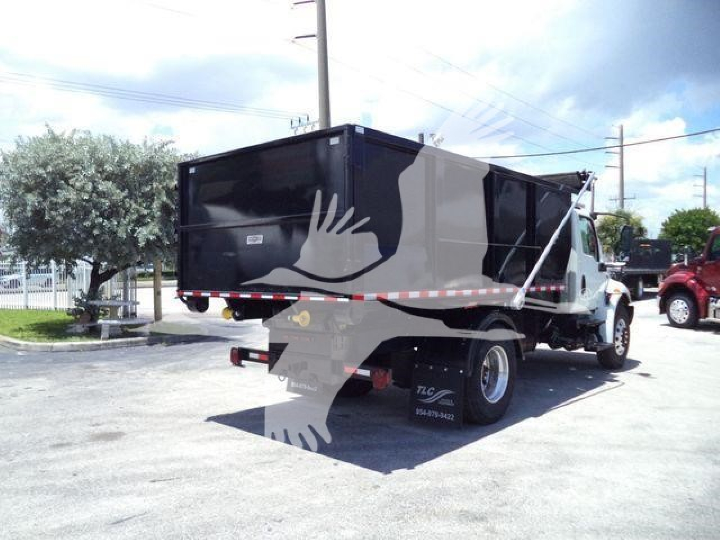 Truck bed with black dump body on International MV roll-off truck, rear view showing taillights and hydraulic system, some white and gray decals.