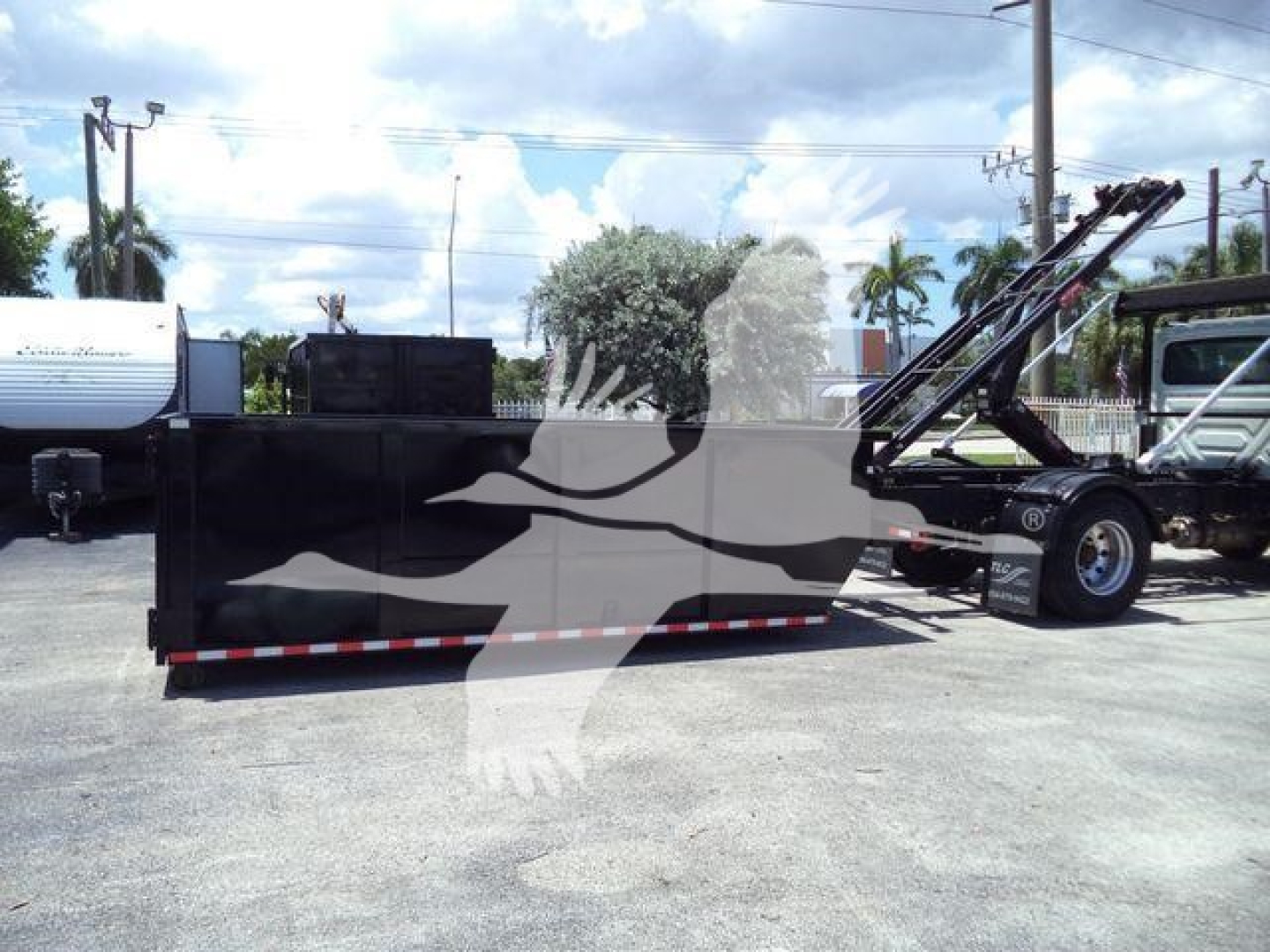 Tractor-style roll-off truck with a large black dump body and hydraulic lifting arm in-side view showing side profile and mounting hardware.