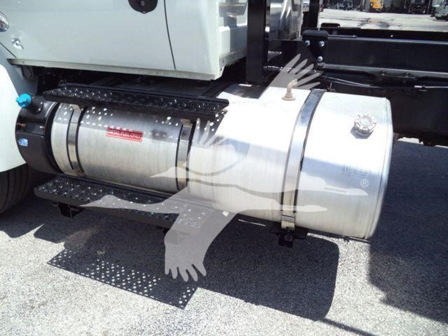 Engine bay showing a stainless steel fuel or storage tank with fittings and a ladder-style step, attached to a white truck chassis.