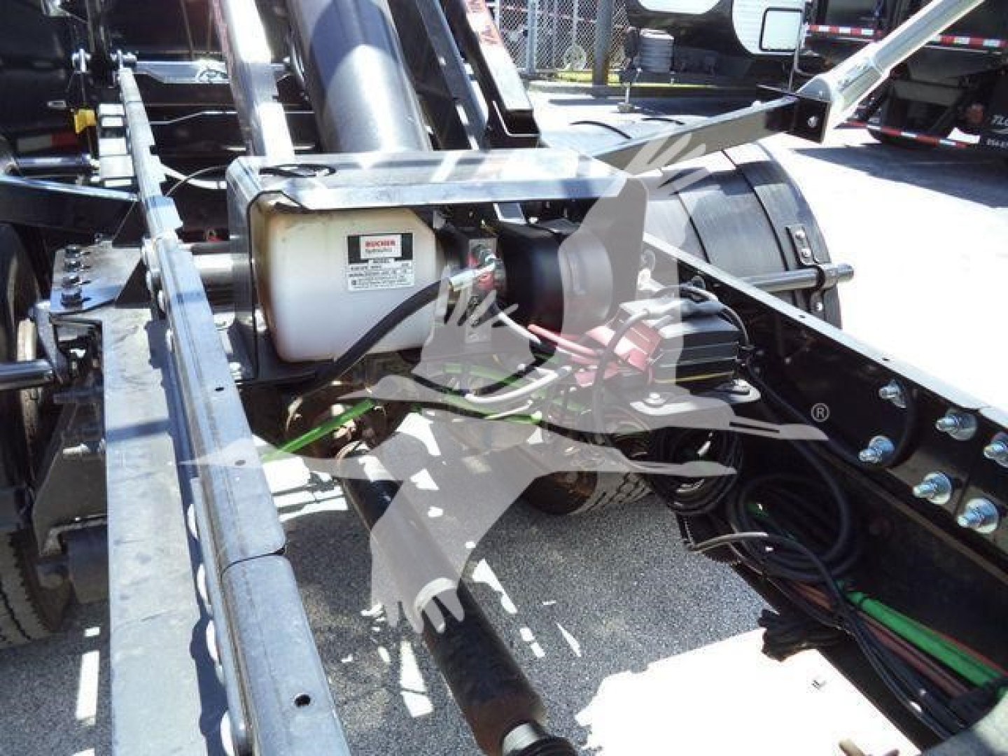 Truck chassis view showing hydraulic reservoir and hydraulic lines with metal frame and suspension components.