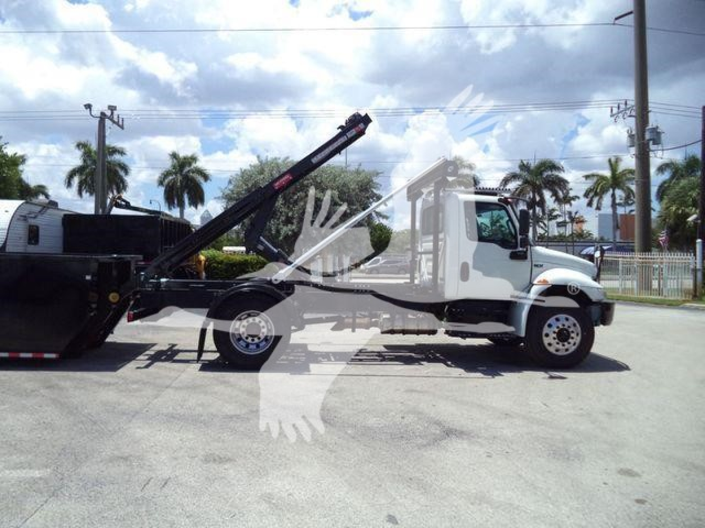 Truck side view of a 2020 International MV roll-off vehicle with a raised hydraulic crane and a linked dumping container.