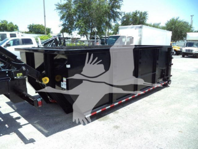 Rolloff truck bed in a yard showing a black dump trailer with reflective red/white safety striping and a hydraulic hookup on the side.