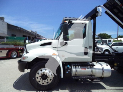 Truck side view of a 2020 International MV roll-off chassis showing cab, fuel tank, and wheel; clear sky and dealership lot in background.