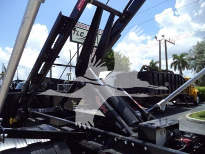 Loader arms and hydraulic controls of a roll-off truck chassis with visible labels and mechanical components.