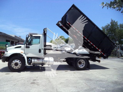 Truck with hydraulic dump bed raised, white cab, black dump bed. Side shows InternationalMV? No clear text. Wheels, chrome exhaust, fuel tanks visible.