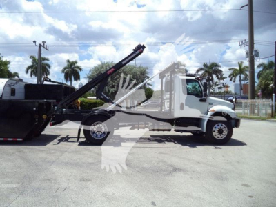Truck side view of a 2020 International MV roll-off vehicle with a raised hydraulic crane and a linked dumping container.
