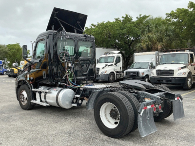 Freightliner Cascadia126 truck cab and chassis view showing cab with open hood and exposed engine bay, side fuel tank, rear dual axle area, and grey mud flaps.