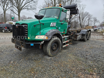 Truck engine bay and front cab of a green 2008 Mack GU813 rolloff truck with black front bumper and exposed chassis.