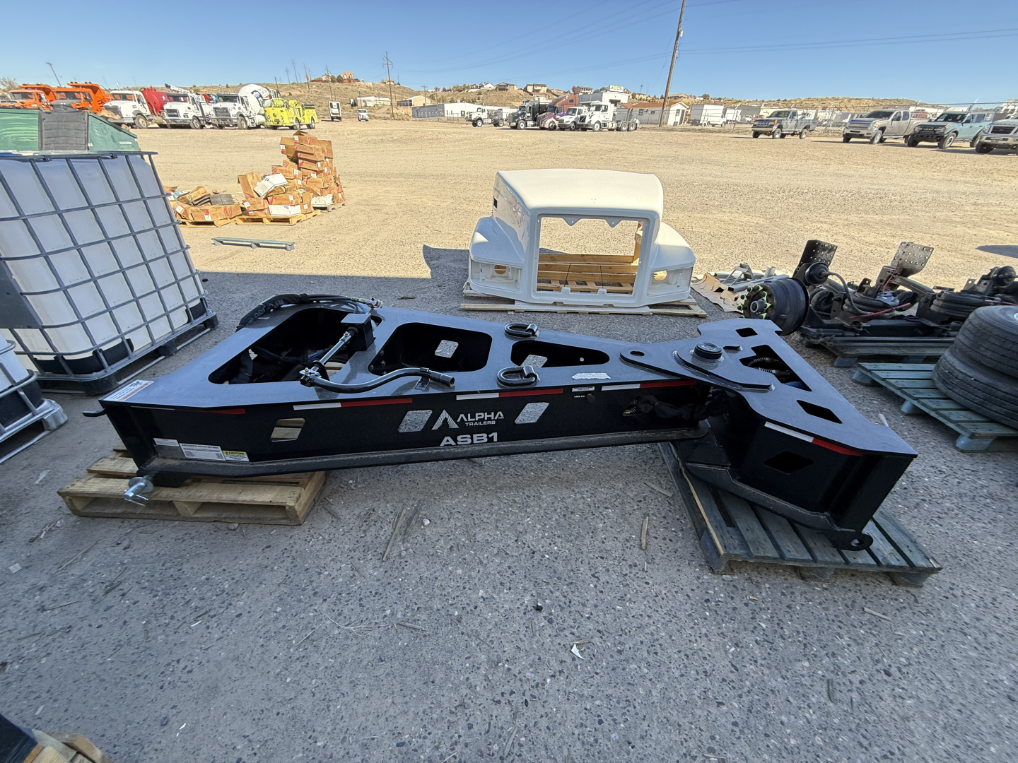 Alpha spreader bar 55 ton 8'-6" trailer frame on ground with surrounding equipment in yard, side view showing frame labeled ALPHA ASB1