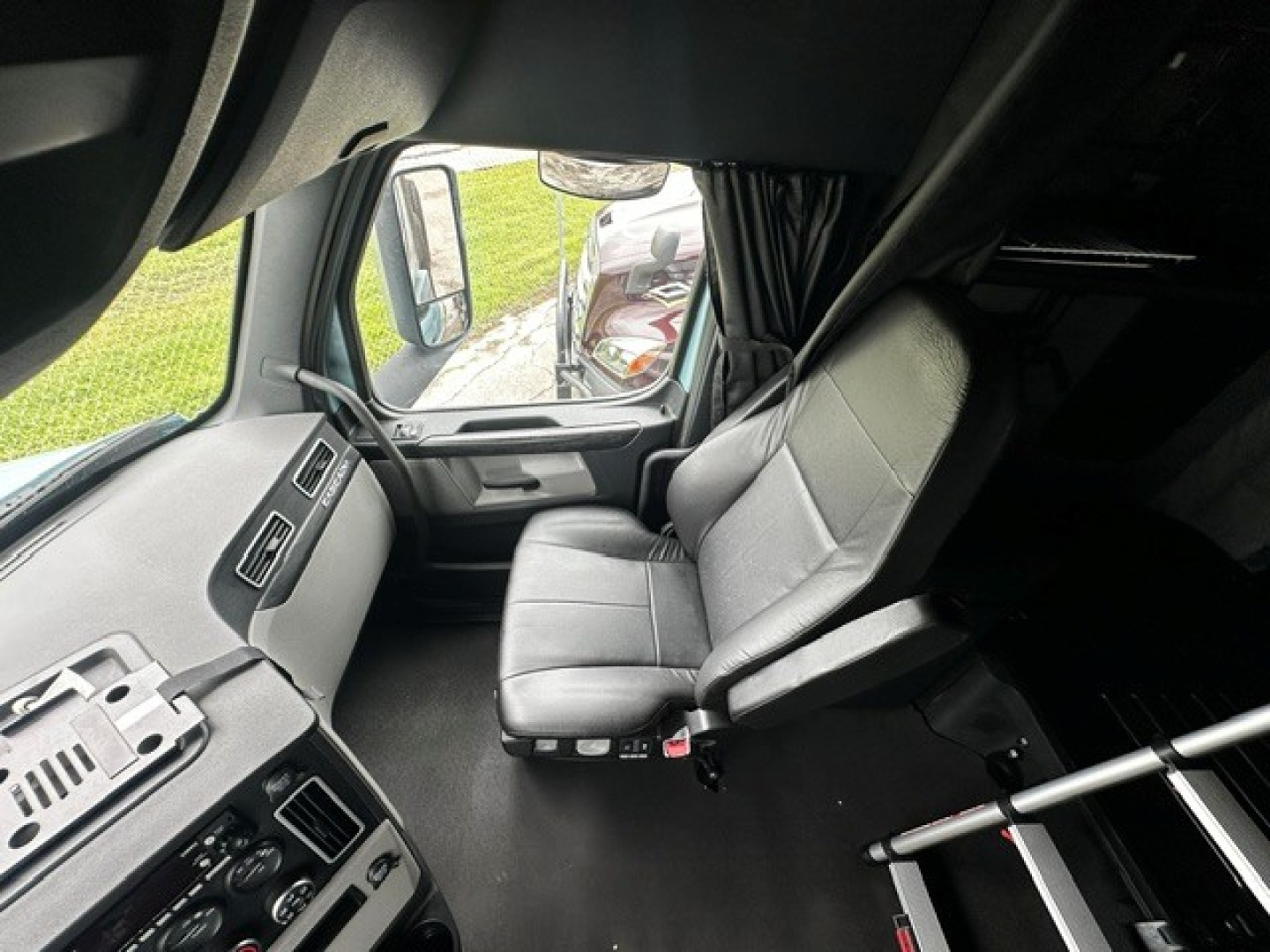 Cab interior of a Freightliner Cascadia 126 truck showing driver's seat and dashboard with controls and side window.