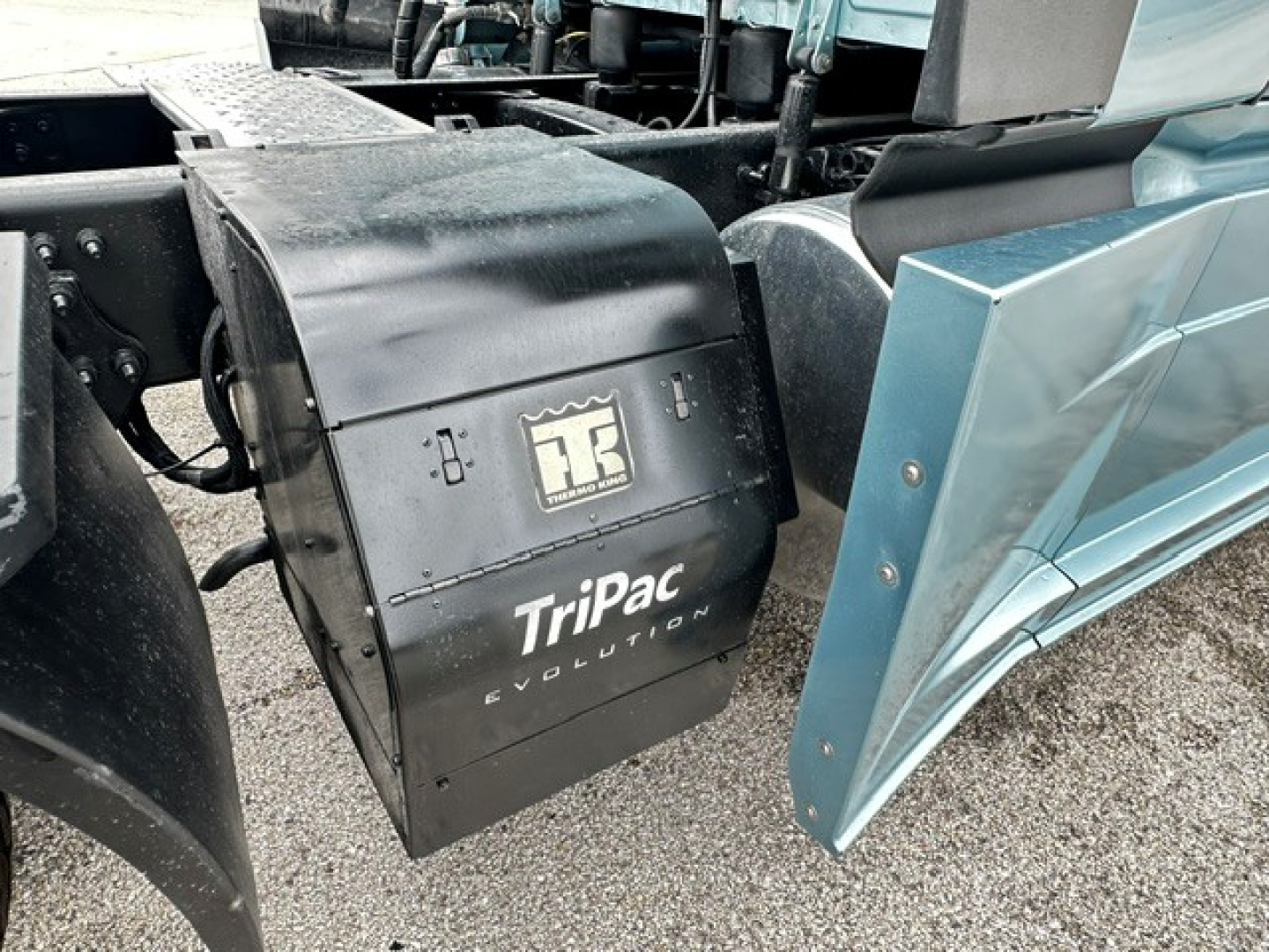 Truck exterior showing TriPac Evolution auxiliary heater/AC unit mounted under a Freightliner Cascadia 126 hood with blue cab panel nearby.