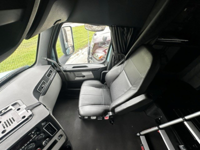 Cab interior of a Freightliner Cascadia 126 truck showing driver's seat and dashboard with controls and side window.