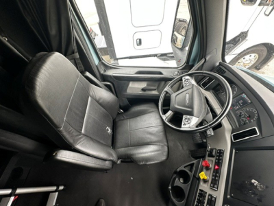 Cab interior of a 2023 Freightliner Cascadia 126 sleeper tractor showing driver seat and steering wheel with control panels and cup holders.
