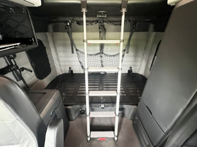 Truck cab interior with ladder extending to sleeper area, cargo floor, netting, and surrounding panels visible inside Freightliner Cascadia 126.