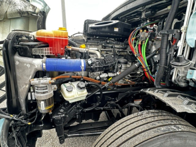 Freightliner Cascadia 126 engine bay showing coolant reservoir, blue silicone hose, oil filter, and exposed wiring harnesses.
