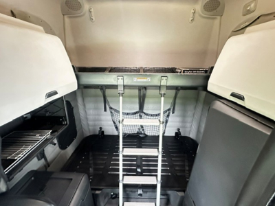 Freightliner Cascadia 126 sleeper cab cargo area with overhead storage and ladder in the back, interior view showing tie-down hooks and side compartments.