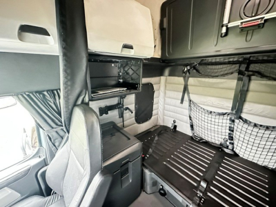 Cab interior of a 2023 Freightliner Cascadia 126 sleeper showing overhead storage cabinet, shelves, and sleeper area with netting and organizational panels.