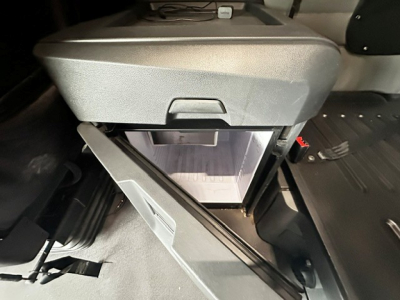 Cab interior showing overhead storage with an open drawer and a small cooler or cabinet in the top center. A drawer front is open revealing empty interior space.