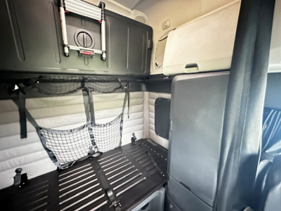 Truck sleeper cab interior with storage net, overhead cabinet, and side panel. No legible text visible on components.