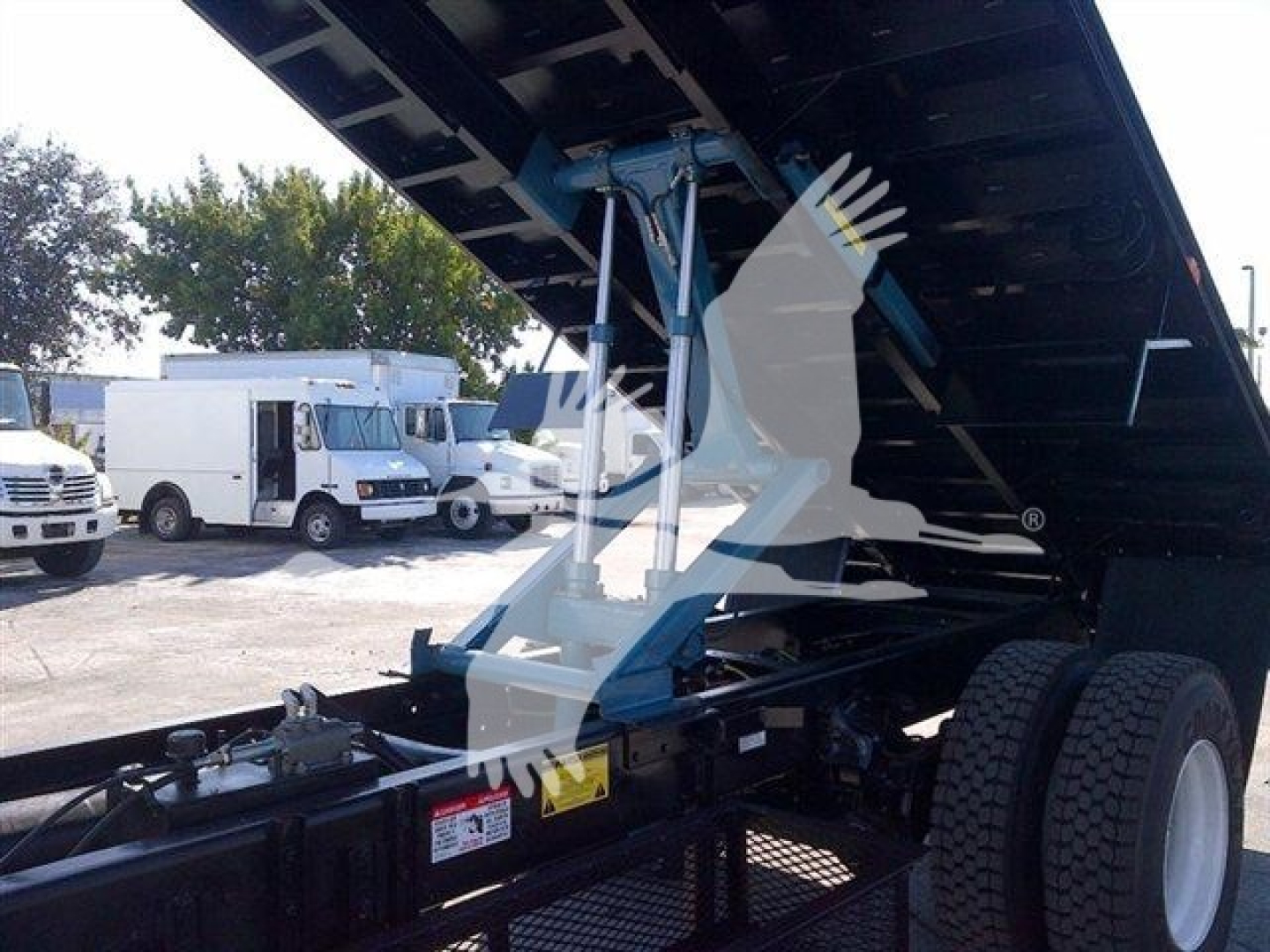 Flatbed truck in raised position showing hydraulic system and undercarriage with tires visible.