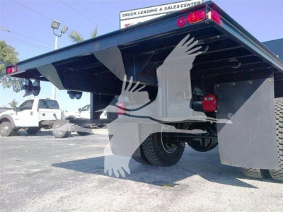 Flatbed truck rear view showing open deck and dual rear wheels under trailer; tail lights and mud flaps visible.