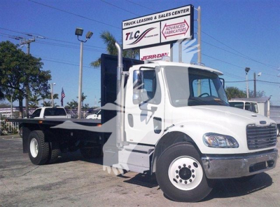 Flatbed truck showing cab and extended frame under a dealership sign.
