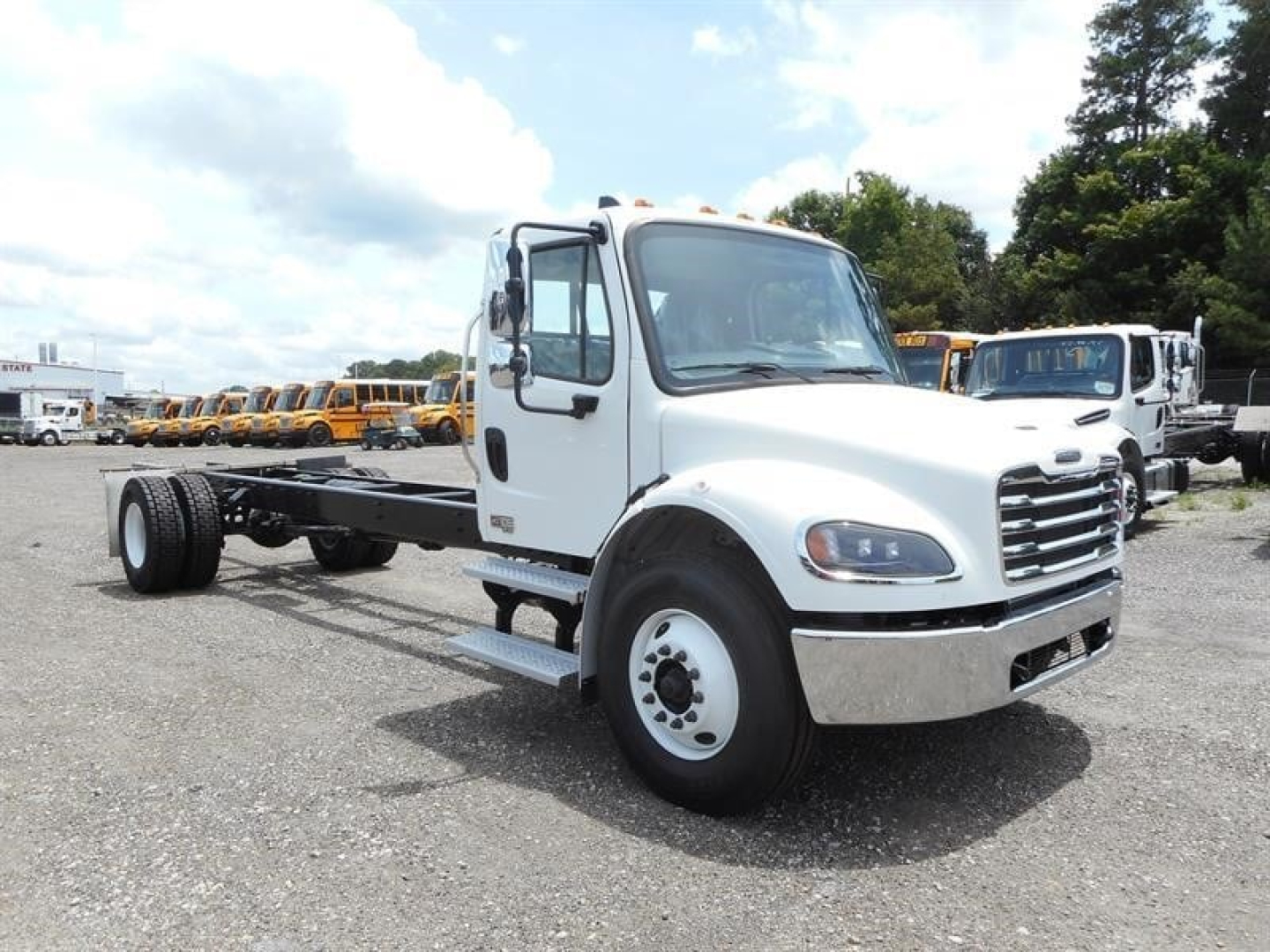 Freightliner M2 106 cab and chassis truck in a dealership lot. Front cab visible with white paint, grille, headlights; extended chassis behind cab with dual rear axles not installed. Stock and VIN may be on listing but not visible on truck.