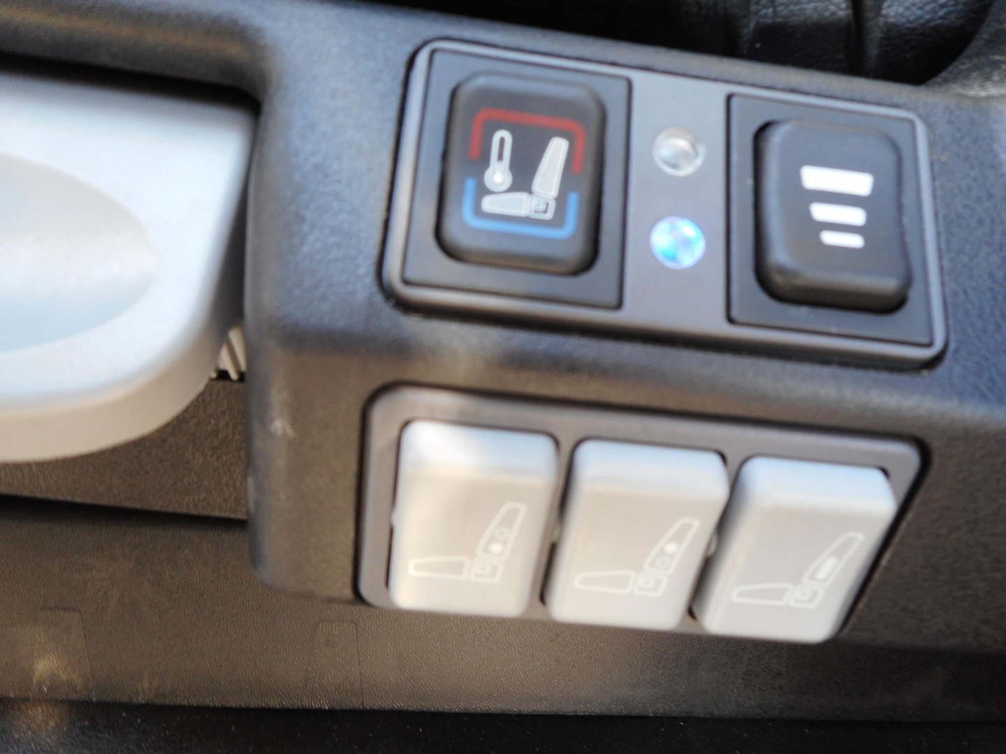 Truck interior switch panel showing three seat adjustment switches and a heated seat icon. Close-up of control buttons on the dashboard.
