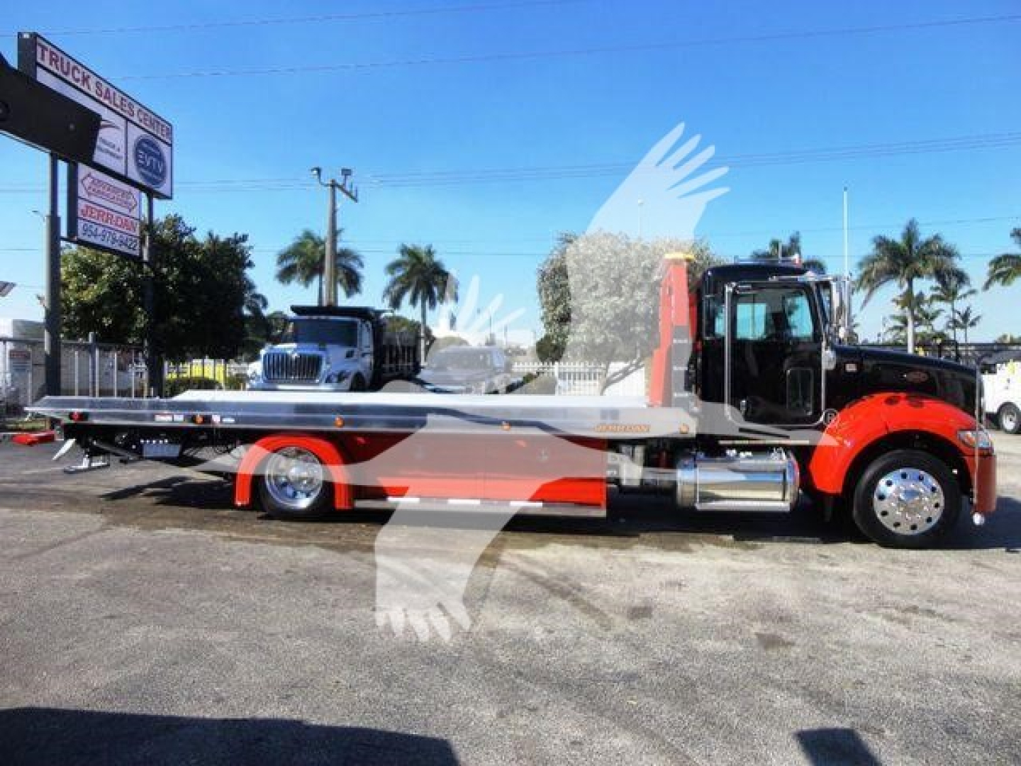 2022 Peterbilt 337 rollback truck side view showing long flatbed, red cab, chrome exhaust, and signage in background.
