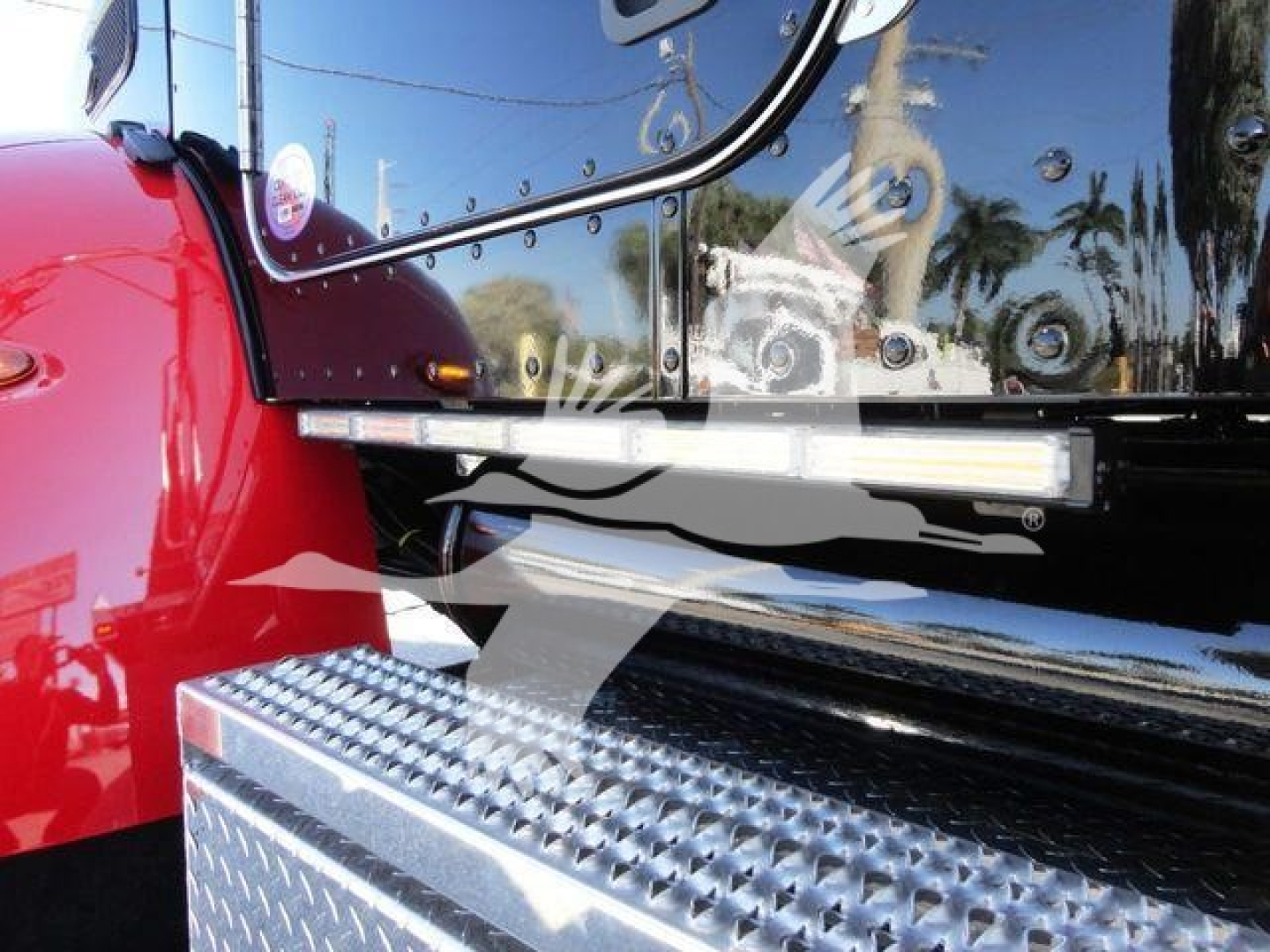 Truck cab side and step panel with diamond plate; reflection of surroundings in chrome mirror and black surface.
