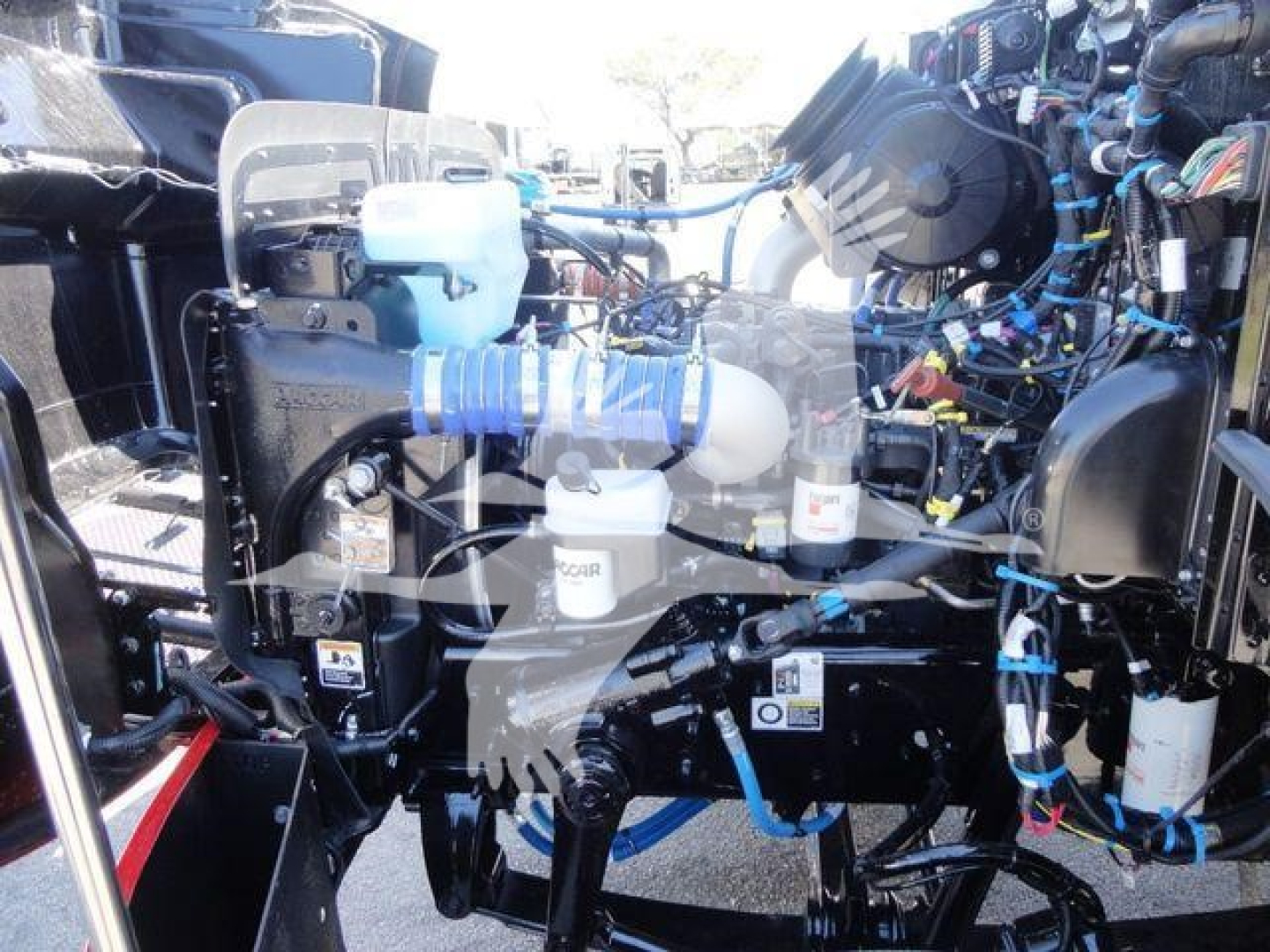 Peterbilt 337 engine bay showing blue coolant reservoir, hoses, wiring, and various engine components in a rollback truck setup.