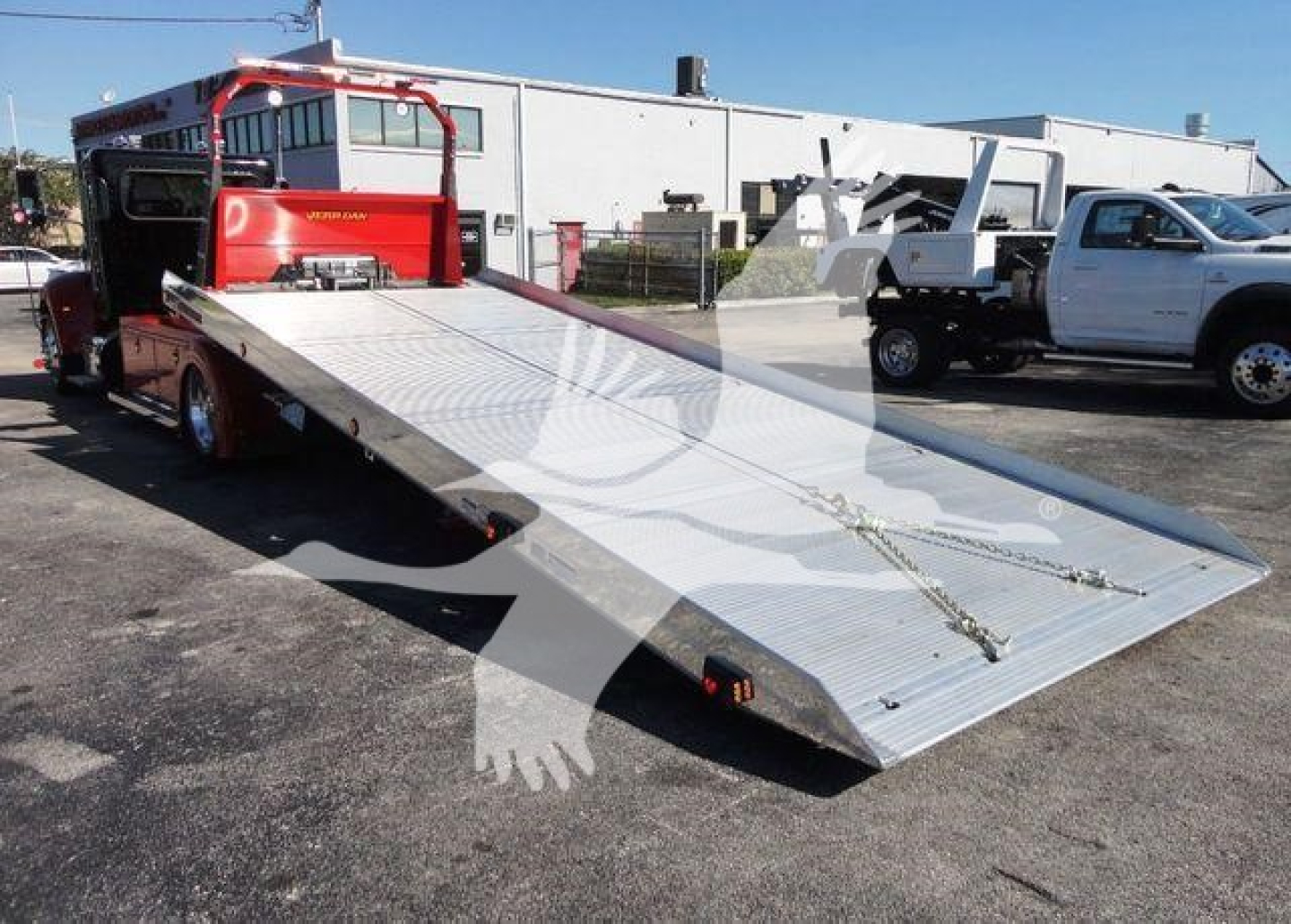 2022 Peterbilt 337 rollback truck with a lowered aluminum flatbed in a dealership lot. Visible text on the truck not legible due to distance.