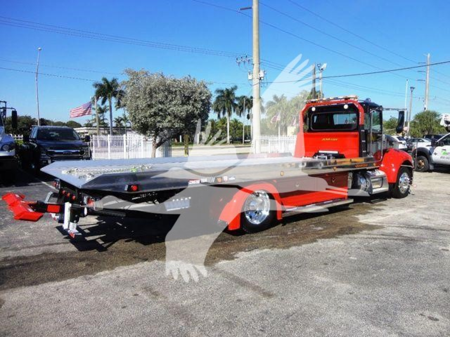 Peterbilt 337 rollback truck with red cab and light-gray flatbed viewed from the side in a dealership lot.